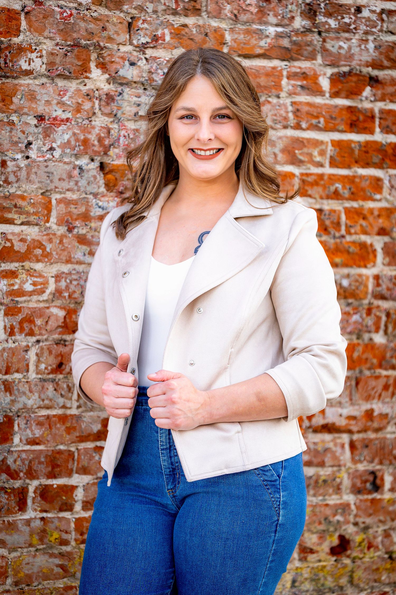 Portrait series against brick wall featuring person in white blazer and blue jeans.