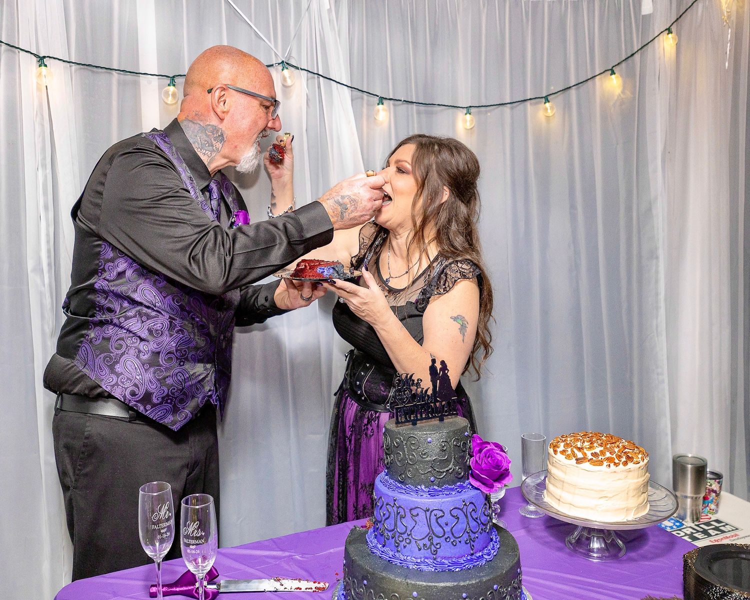 Elegant purple and black wedding cake being cut during reception celebration.