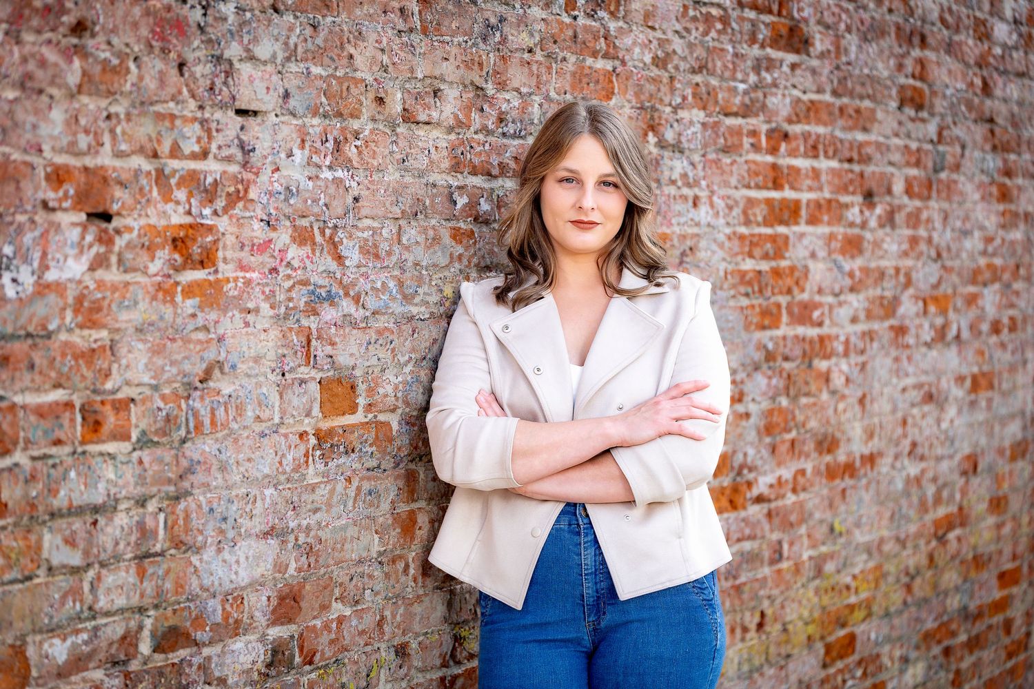 Fashion portrait against weathered brick wall wearing cream blazer and denim.