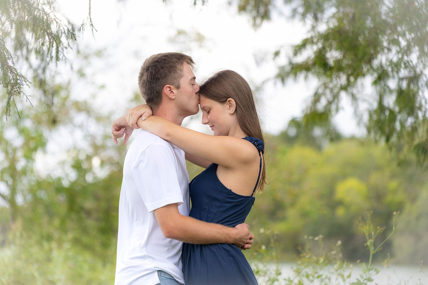 Romantic couple embracing outdoors in soft natural lighting.