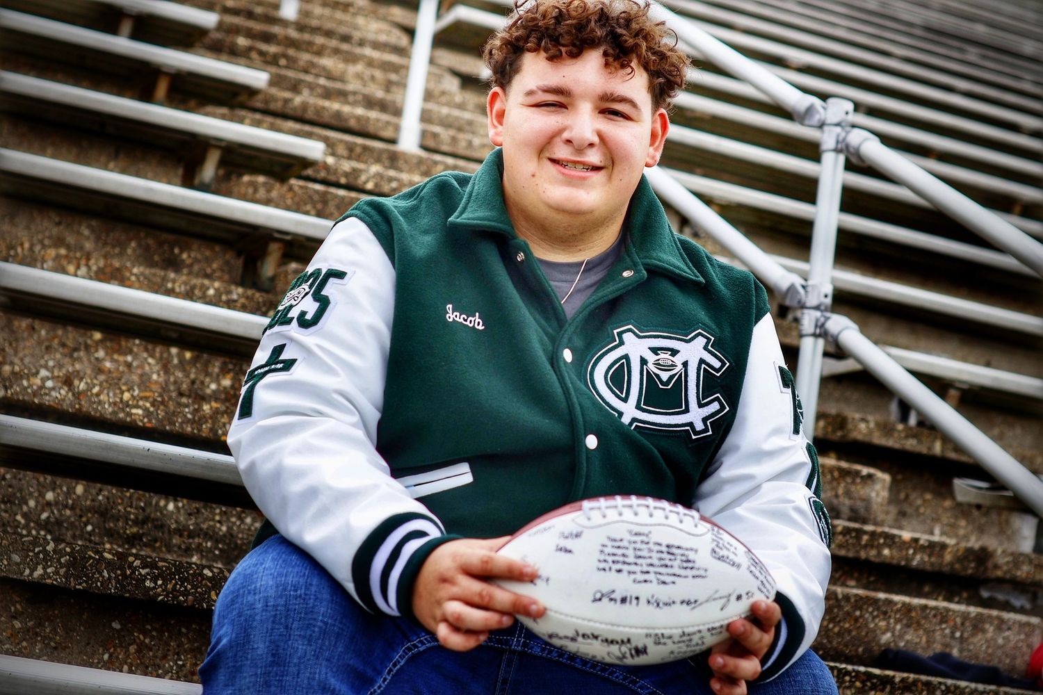 A student sits on stadium bleachers holding a football.