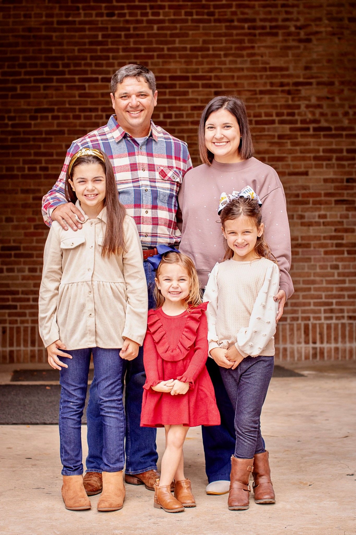 Family of five poses together against brick wall background.