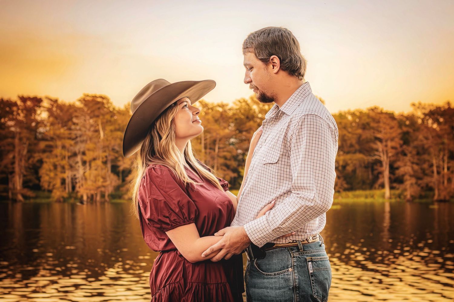 Romantic couple embraces during golden hour sunset by a lake creating a warm silhouetted portrait.