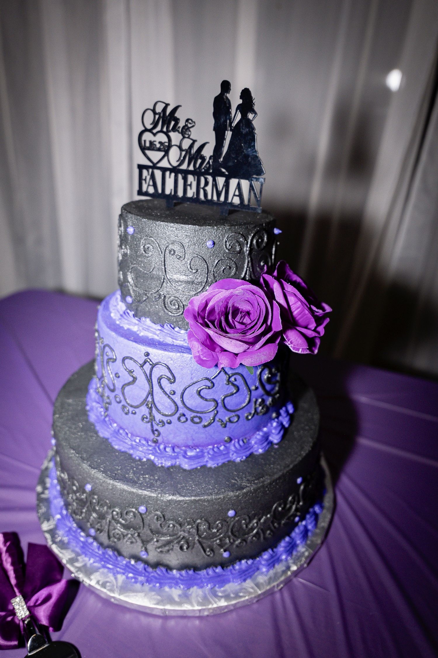 Elegant wedding cake with purple and silver details featuring decorative silhouette topper.