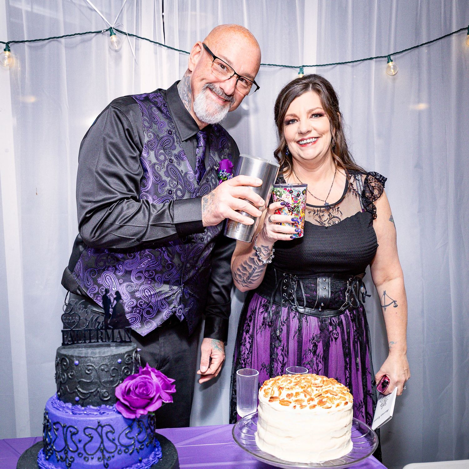 Couple celebrating with purple gothic wedding cake and string lights at reception.