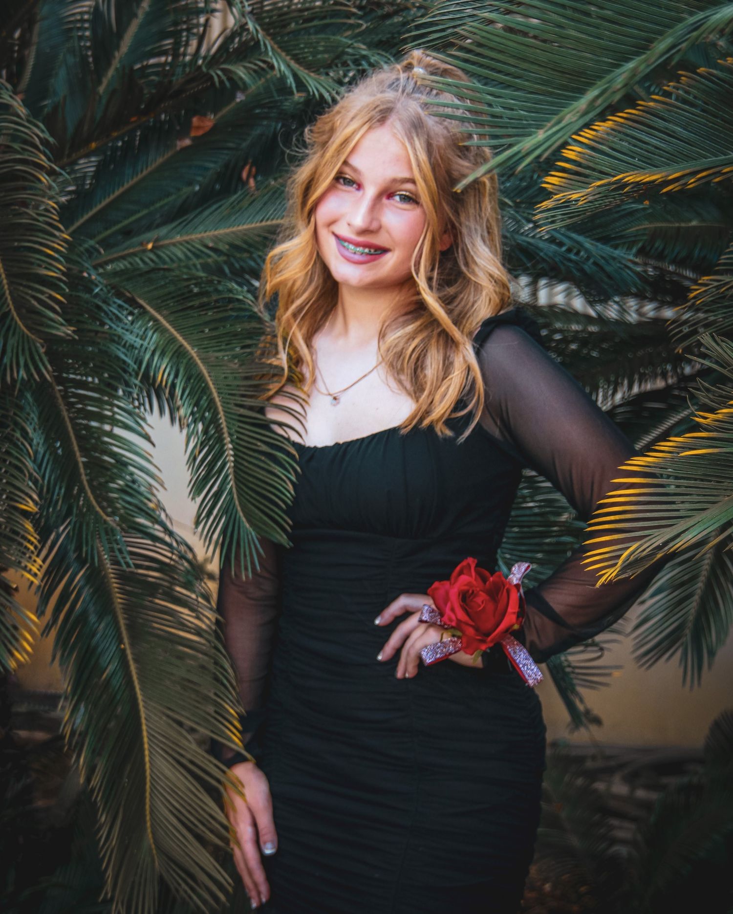 Woman in black dress poses elegantly among tropical palm fronds at sunset.