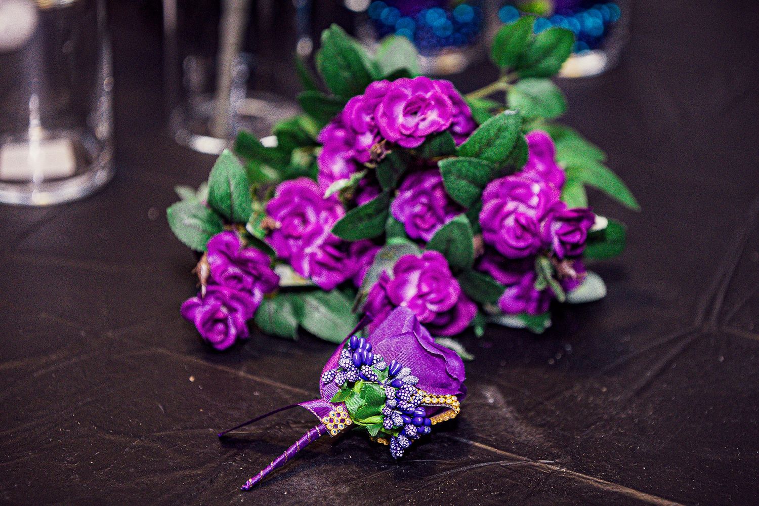 Purple floral arrangements with roses and greenery displayed on dark surface.