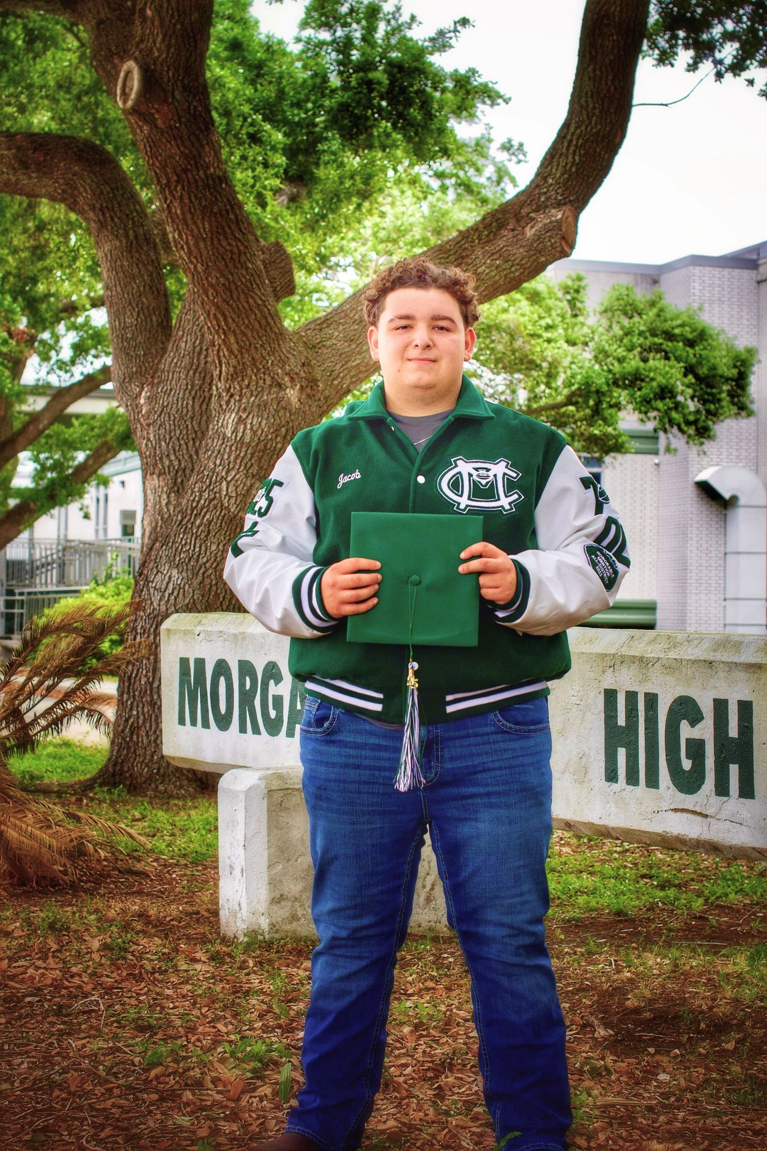 Student in varsity jacket holding folder stands in front of Morgan High School sign.