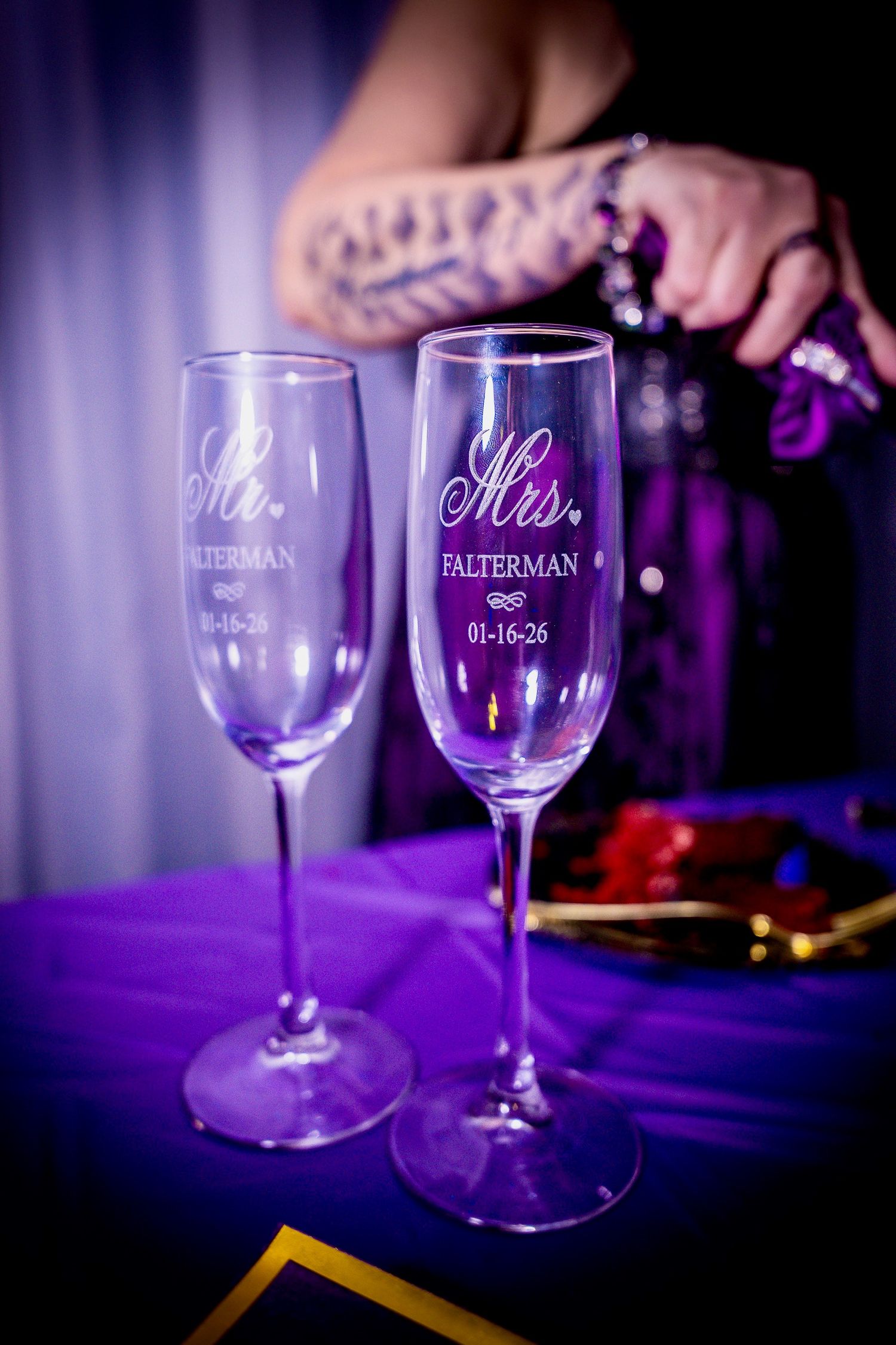 Elegant wine glasses with custom engraving displayed on a purple tablecloth under dramatic lighting.