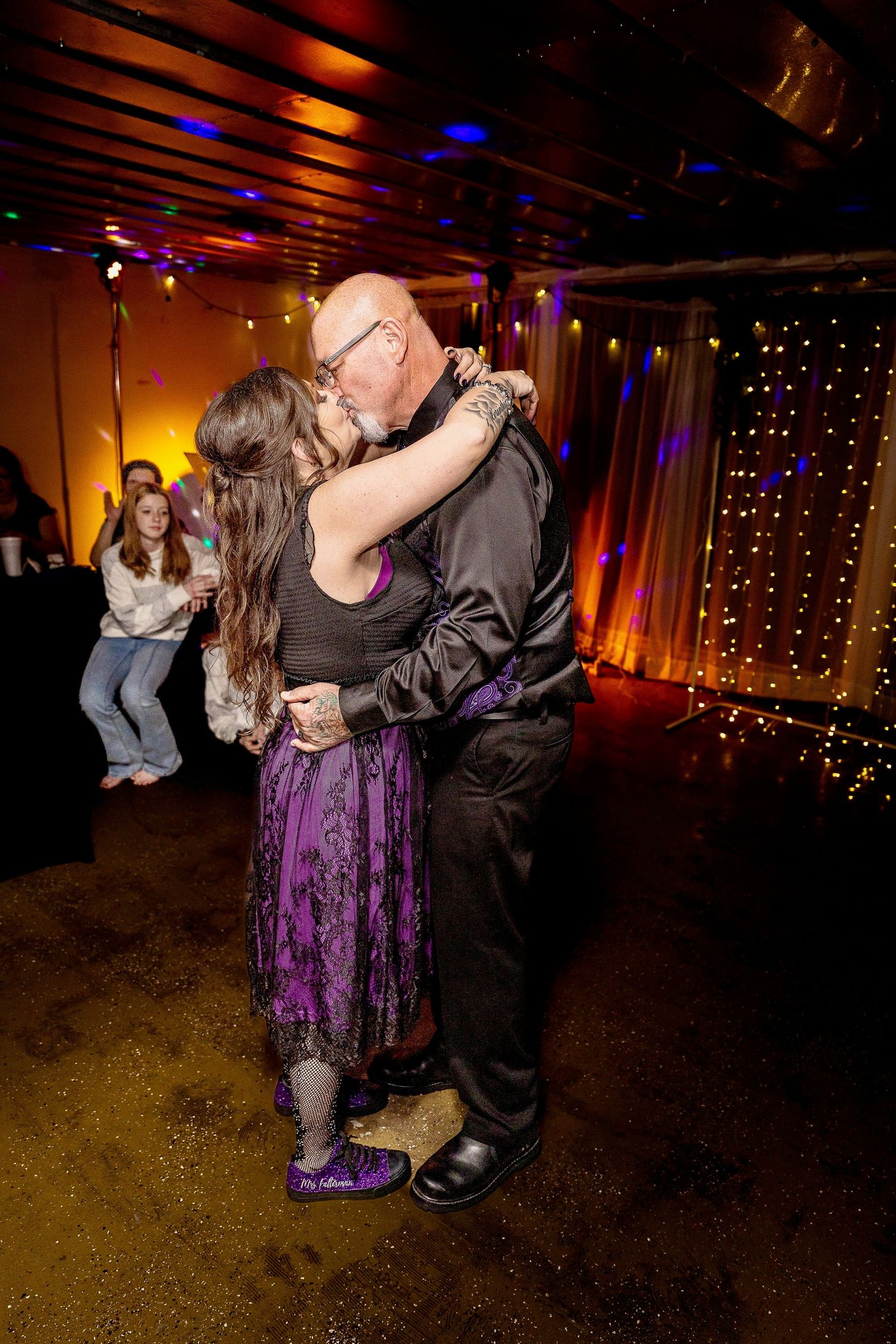 Couples slow dancing in a dimly lit room decorated with string lights.