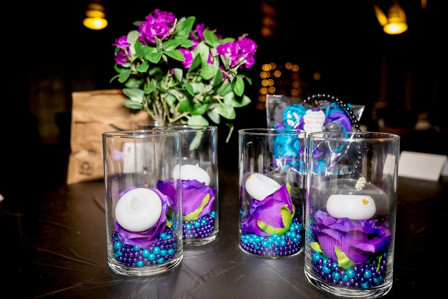 Glass candle holders decorated with purple flowers and blue accents on dark table.