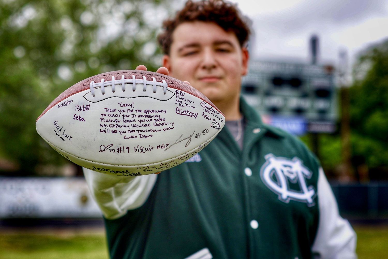 A student displays signed footballs while sitting on outdoor bleachers.