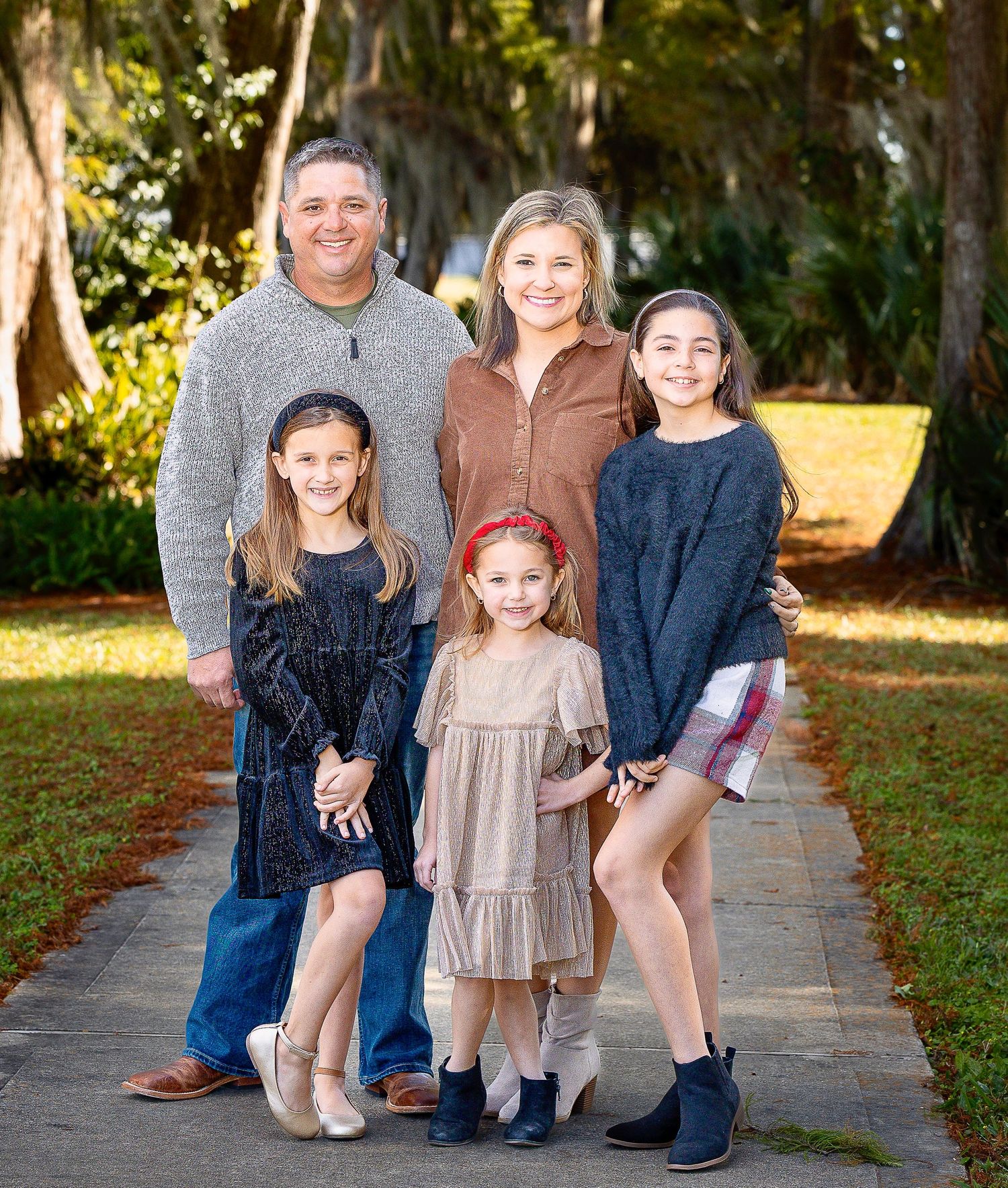Casual family photo session outdoors on stone walkway with trees in background.