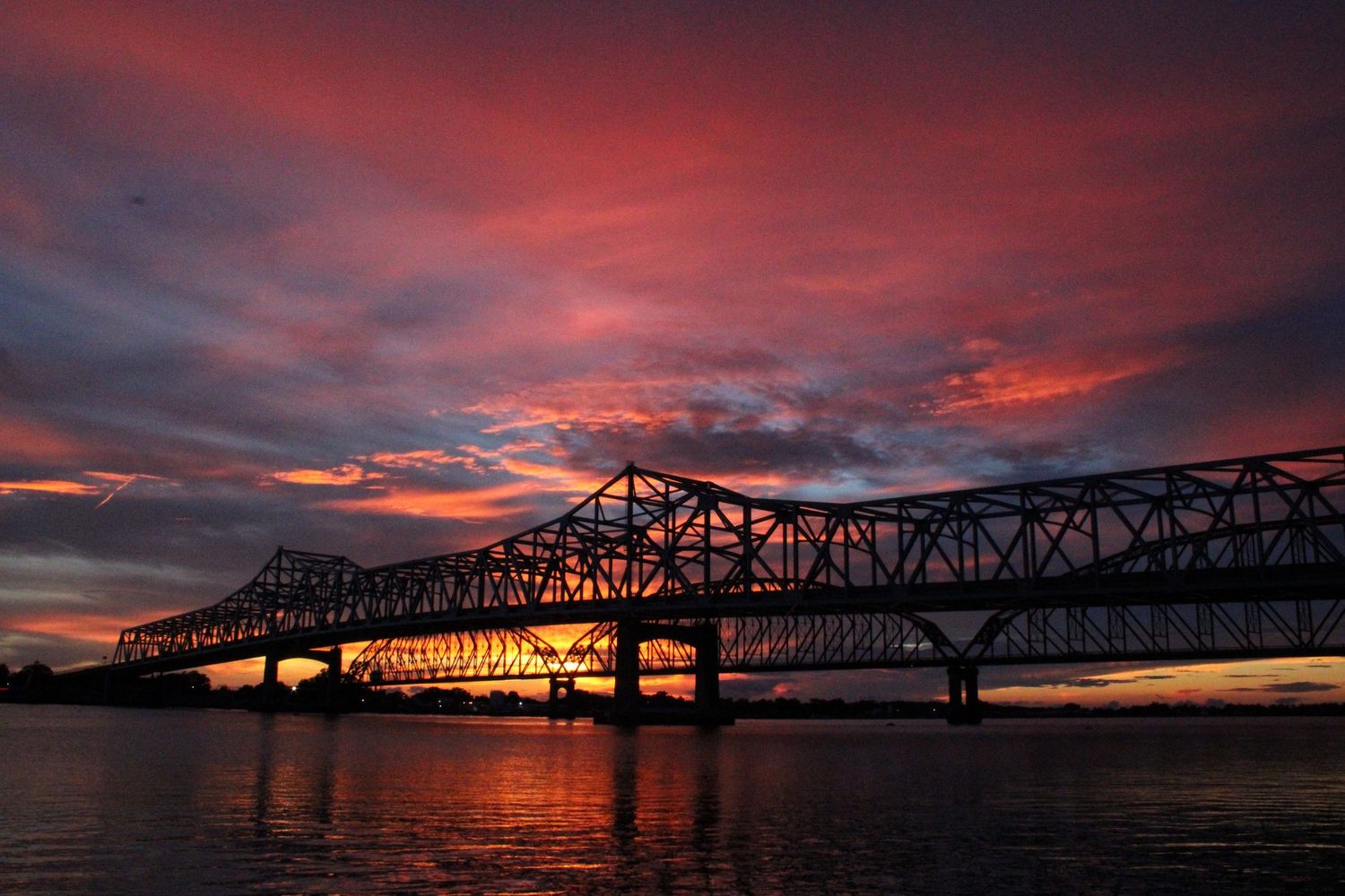 Panoramic sunset view of railroad bridge silhouetted against dramatic red and purple sky.