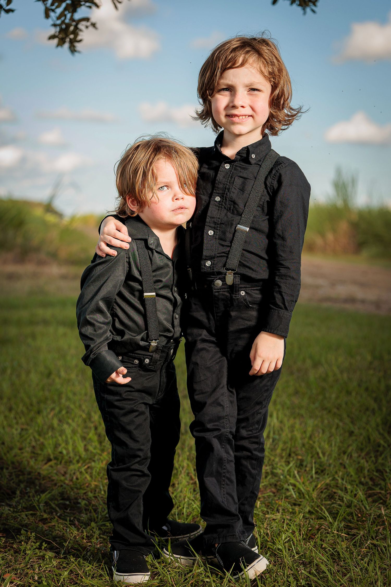 Two children in matching black denim outfits play together in grassy field.