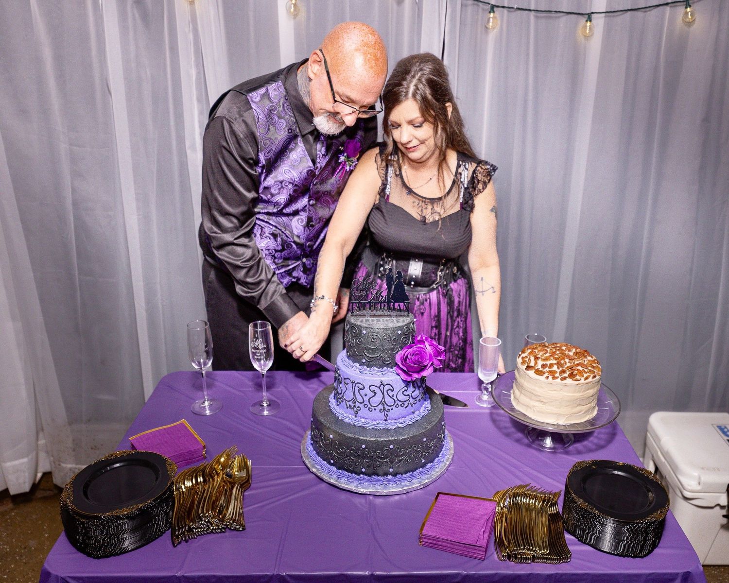 Wedding couple cutting into a purple and black tiered cake at their reception celebration.