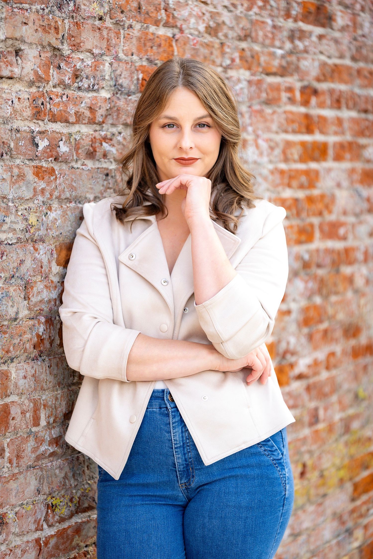 Portrait against weathered brick wall wearing light blazer and jeans.