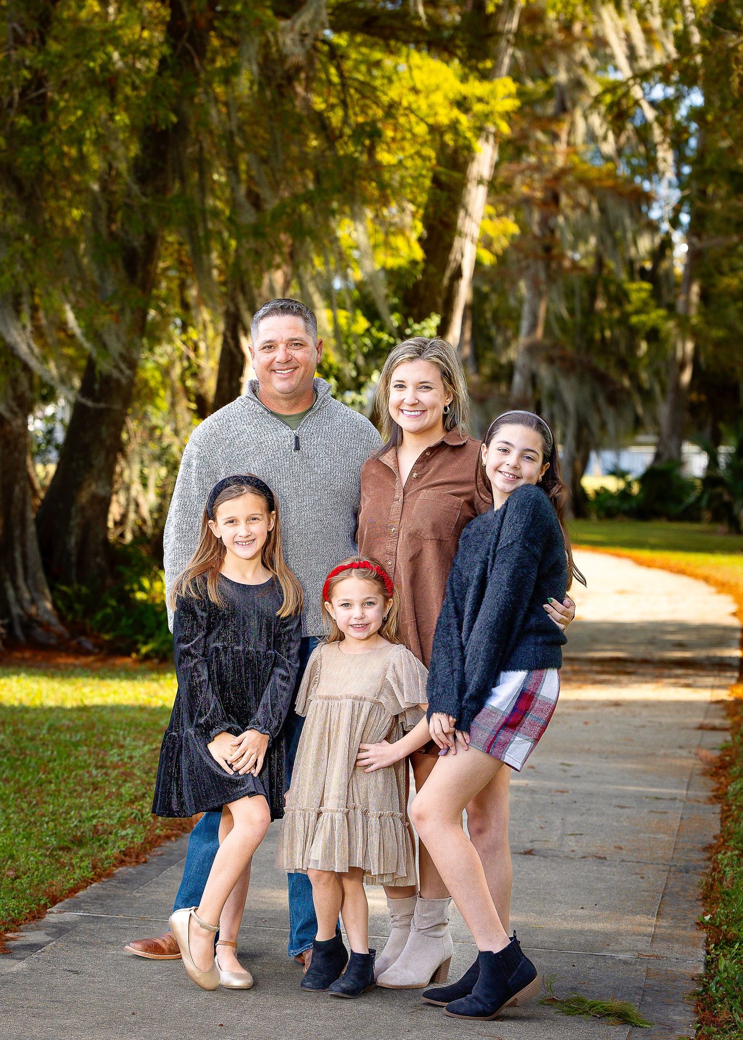 Family group portrait on tree-lined path in outdoor park setting.