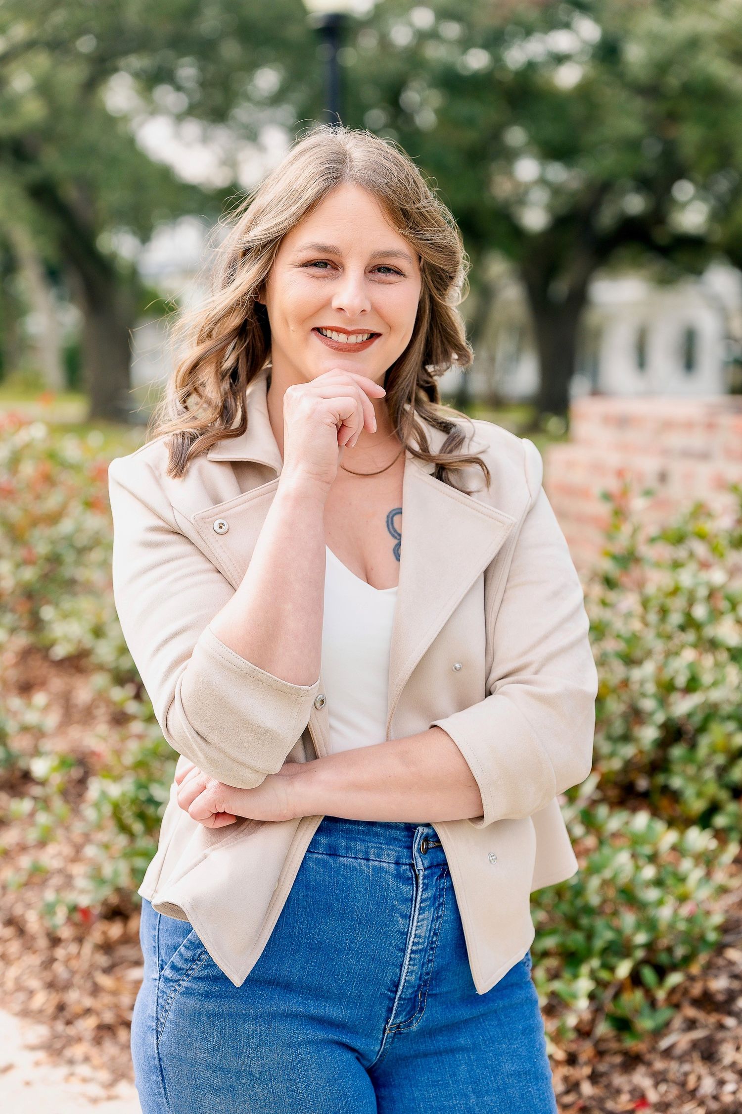 Portrait session featuring cream blazer and jeans against floral garden background.