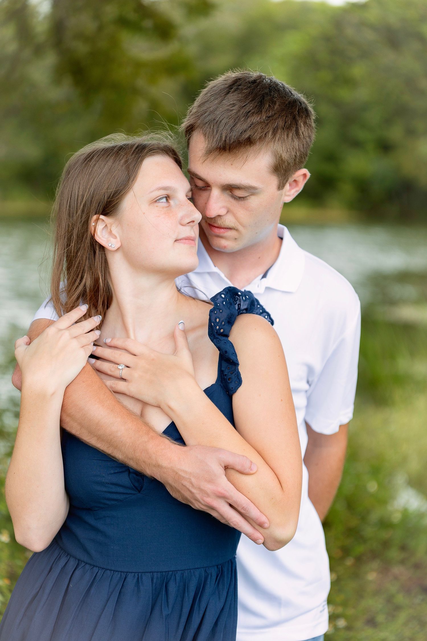 Romantic outdoor portrait of a couple embracing by a lake in casual attire.