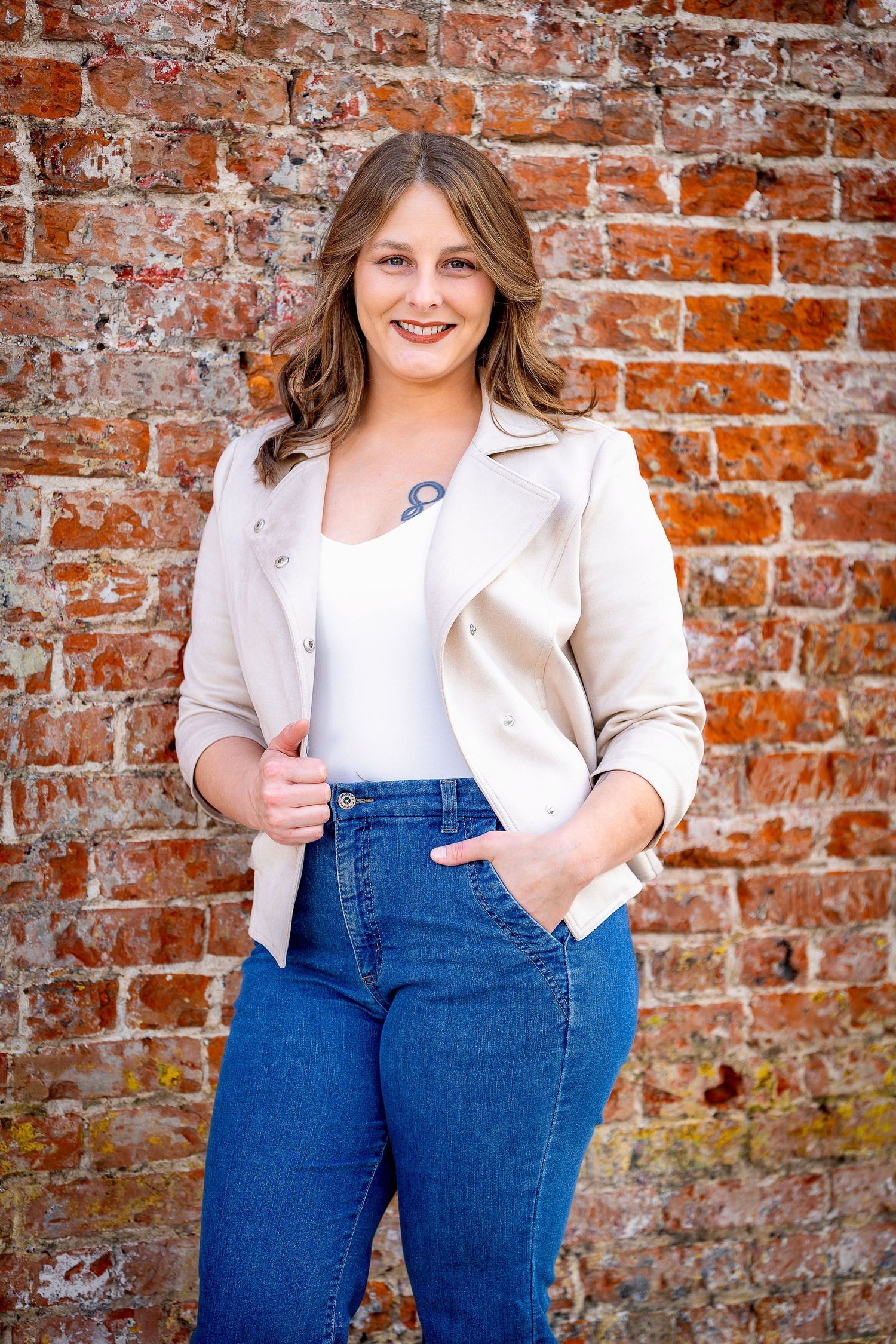 Casual professional portrait against brick wall wearing light blazer and jeans.