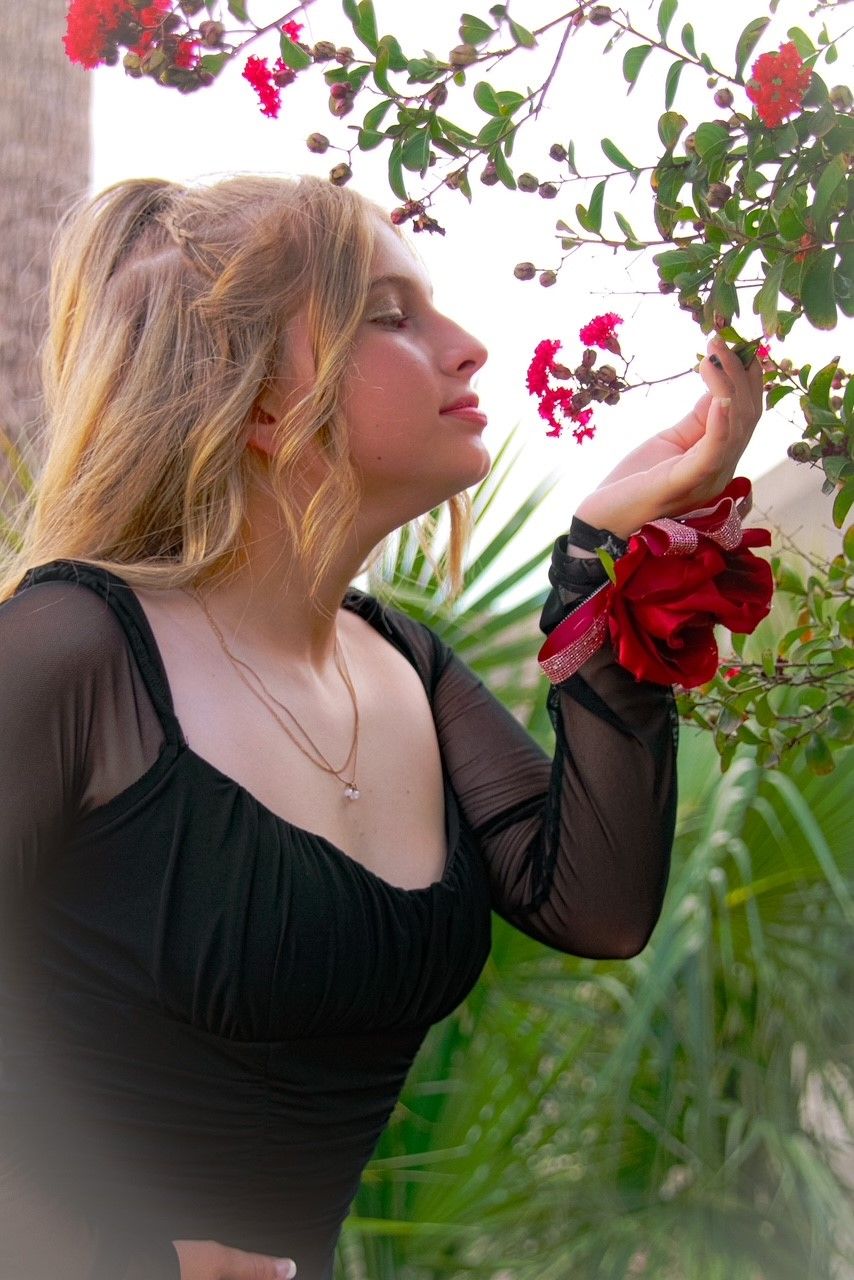 Woman in black dress admiring blooming red flowers in a garden setting.