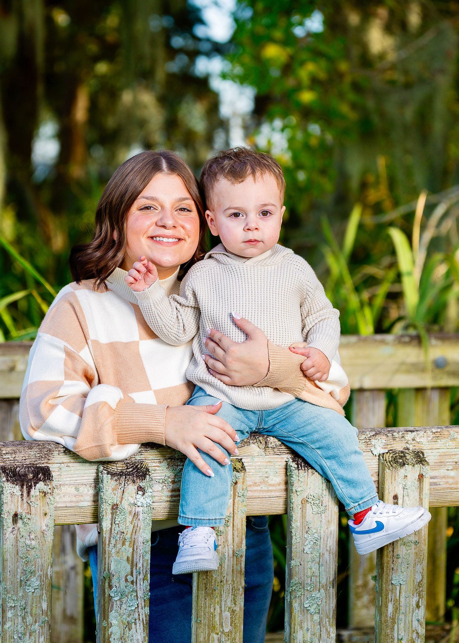 Parent and child share tender moments while sitting on rustic wooden fence in garden setting.