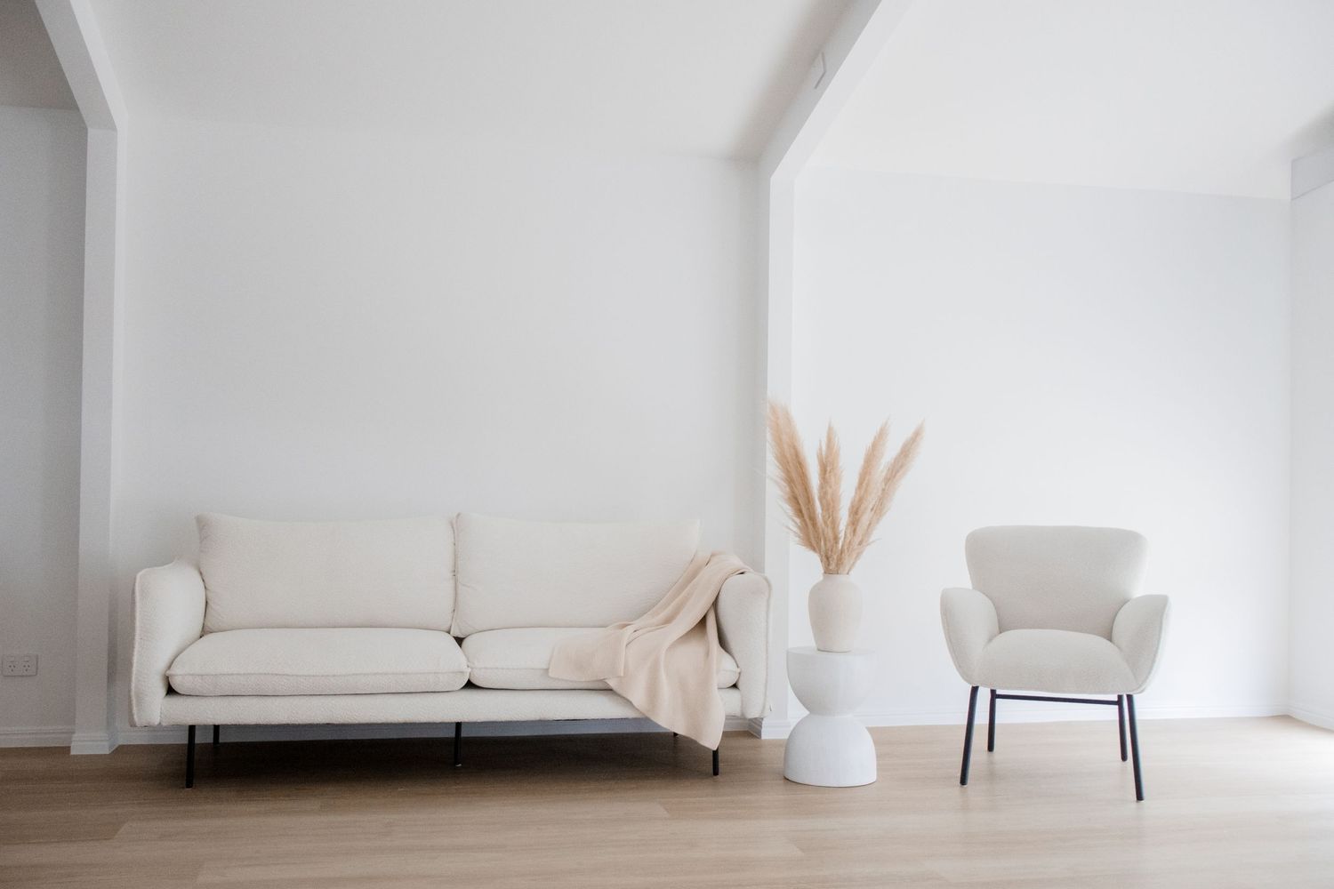 Airy white living room featuring a cream couch, bouclé chair, and pampas grass in tall vase.
