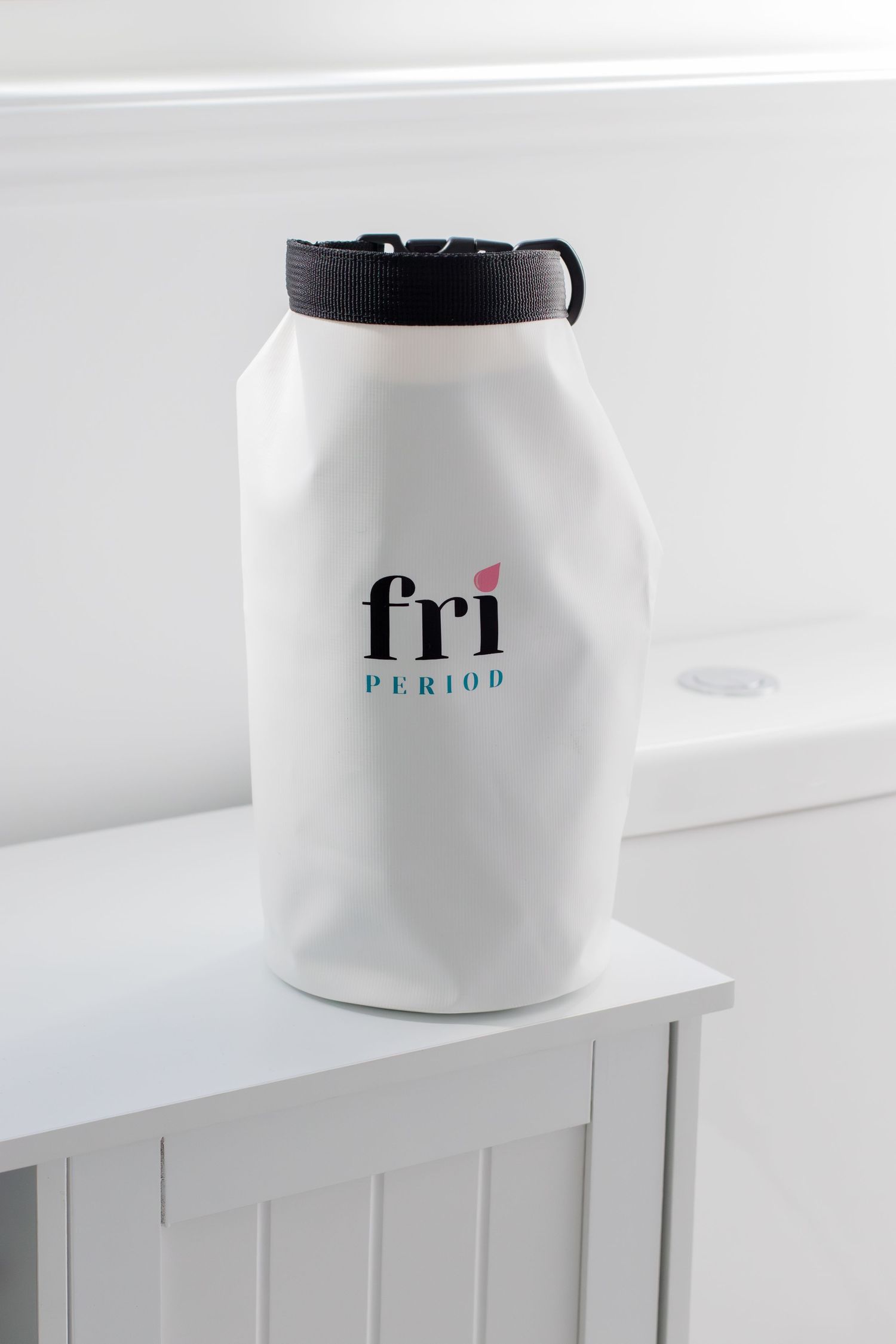 White Fri Period branded waterproof dry bag with black closure sitting on white bathroom cabinet.