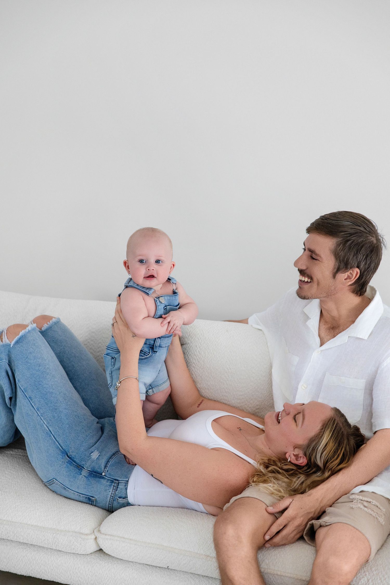 Joyful family moment with parents and baby in blue denim outfit on white couch.