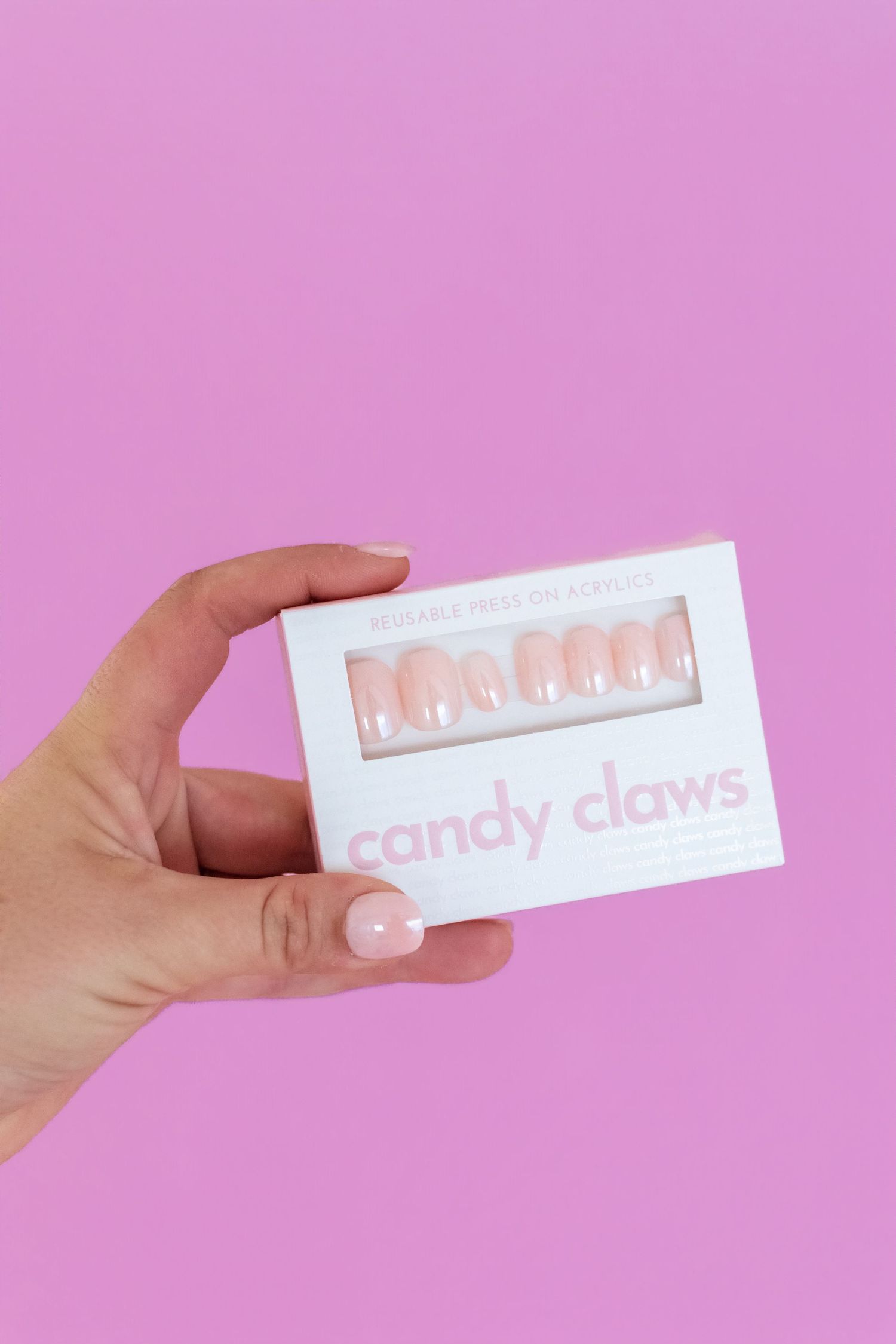 Hand holding Candy Claws reusable press-on nails box in soft pink on a pink background.