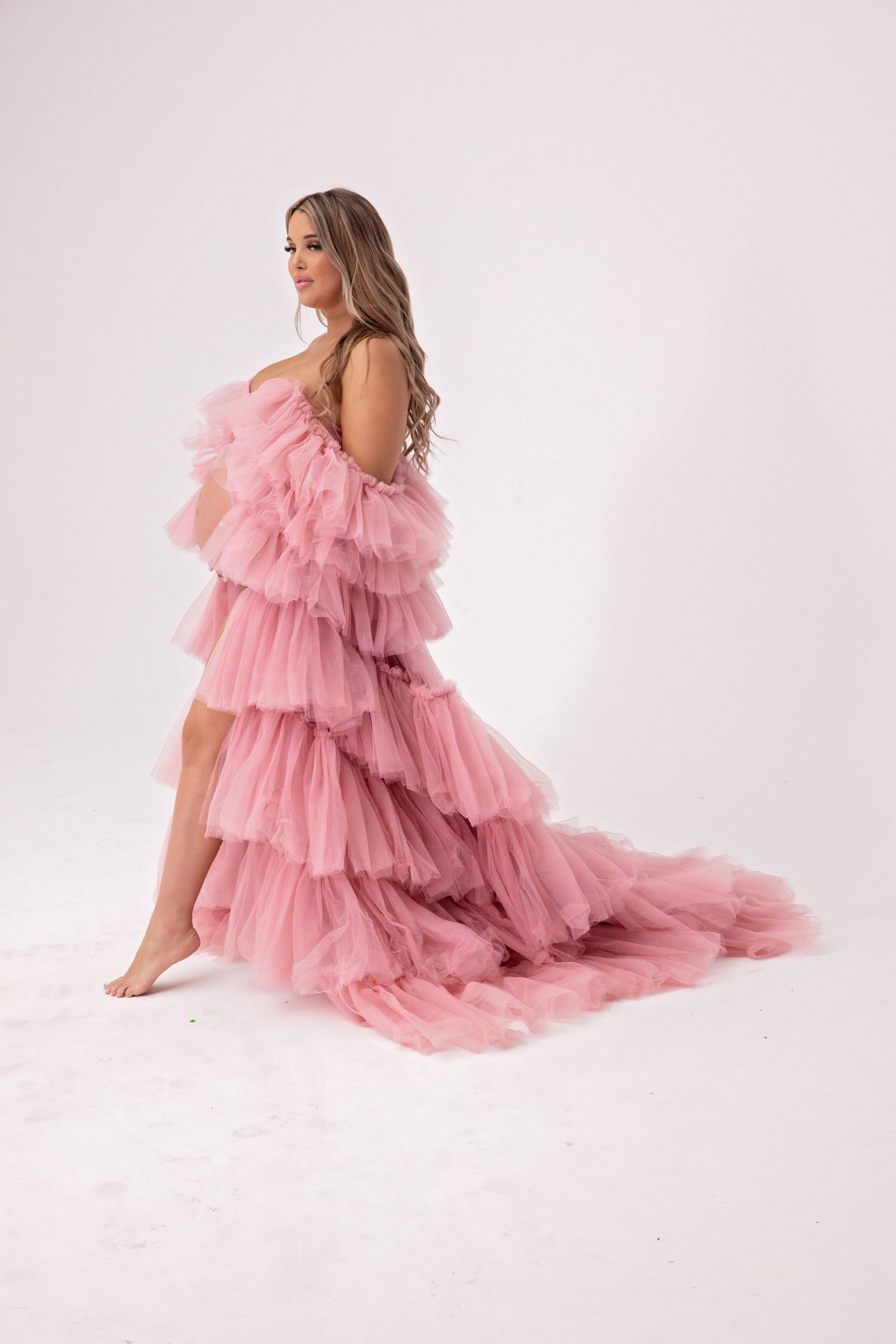 Woman posing in elegant layered pink tulle ruffle gown on white studio background.