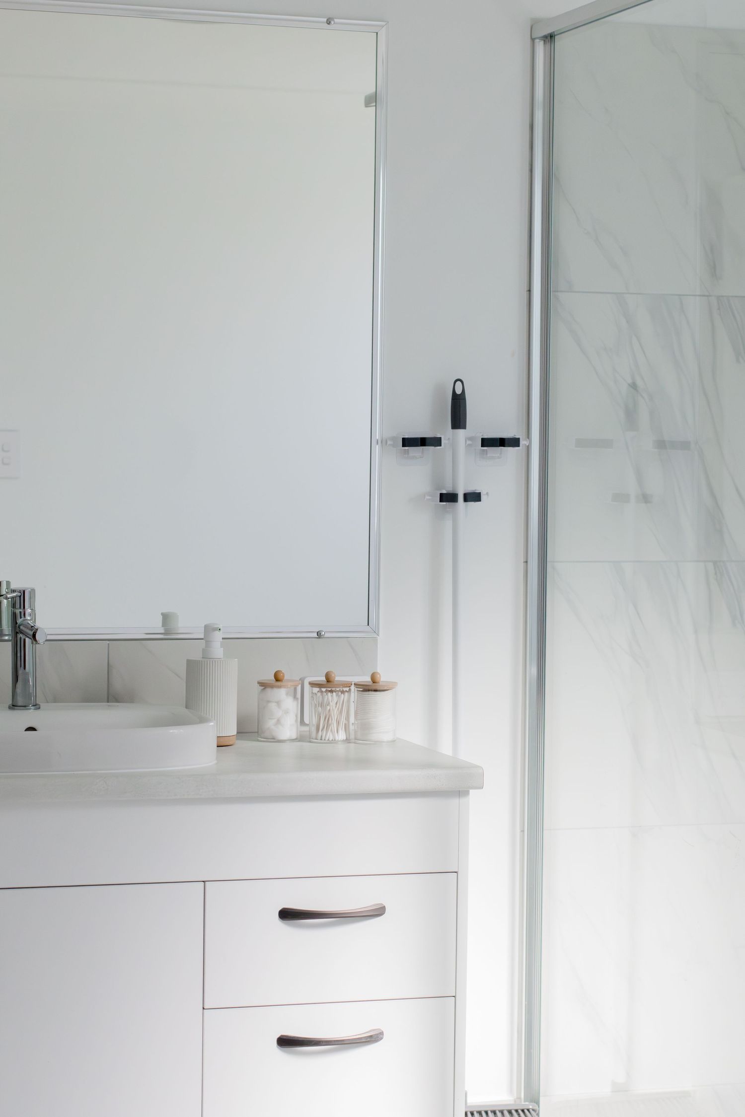 Modern white bathroom vanity with mirror, marble countertop, and glass shower door.