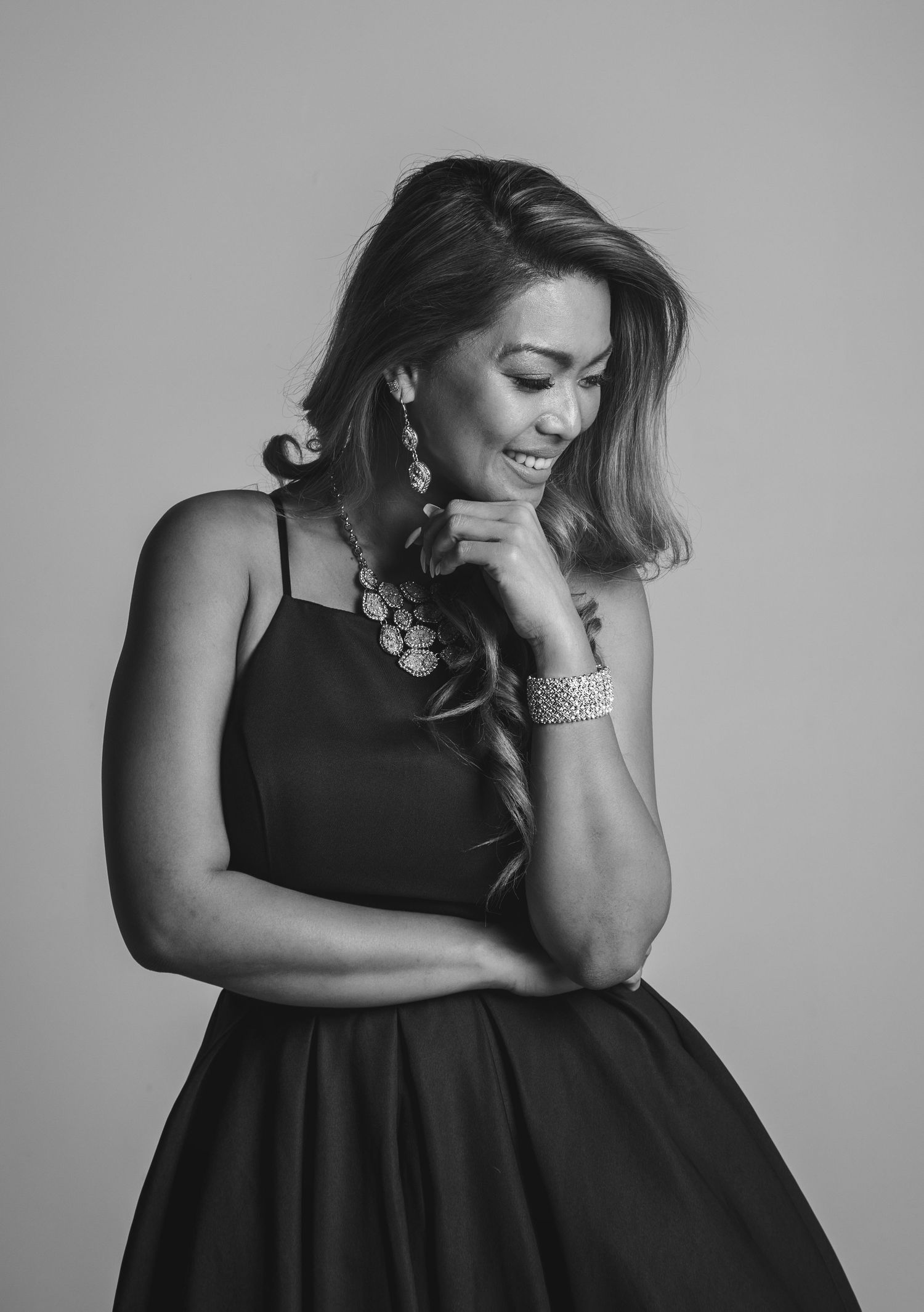 Black and white portrait of elegant woman in black dress with statement jewelry smiling.