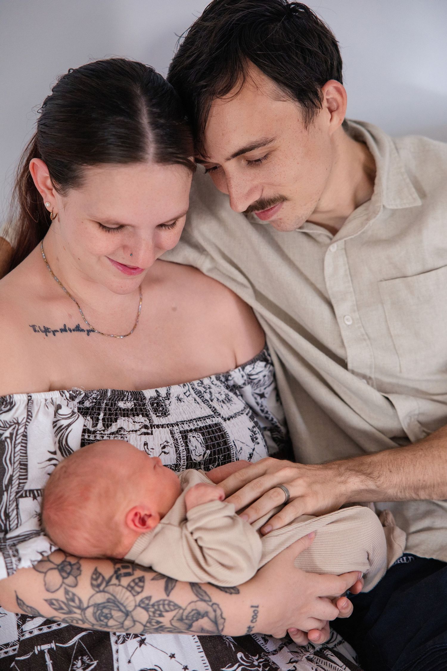 Young couple with tattoos tenderly gazing at their newborn baby wrapped in a blanket.