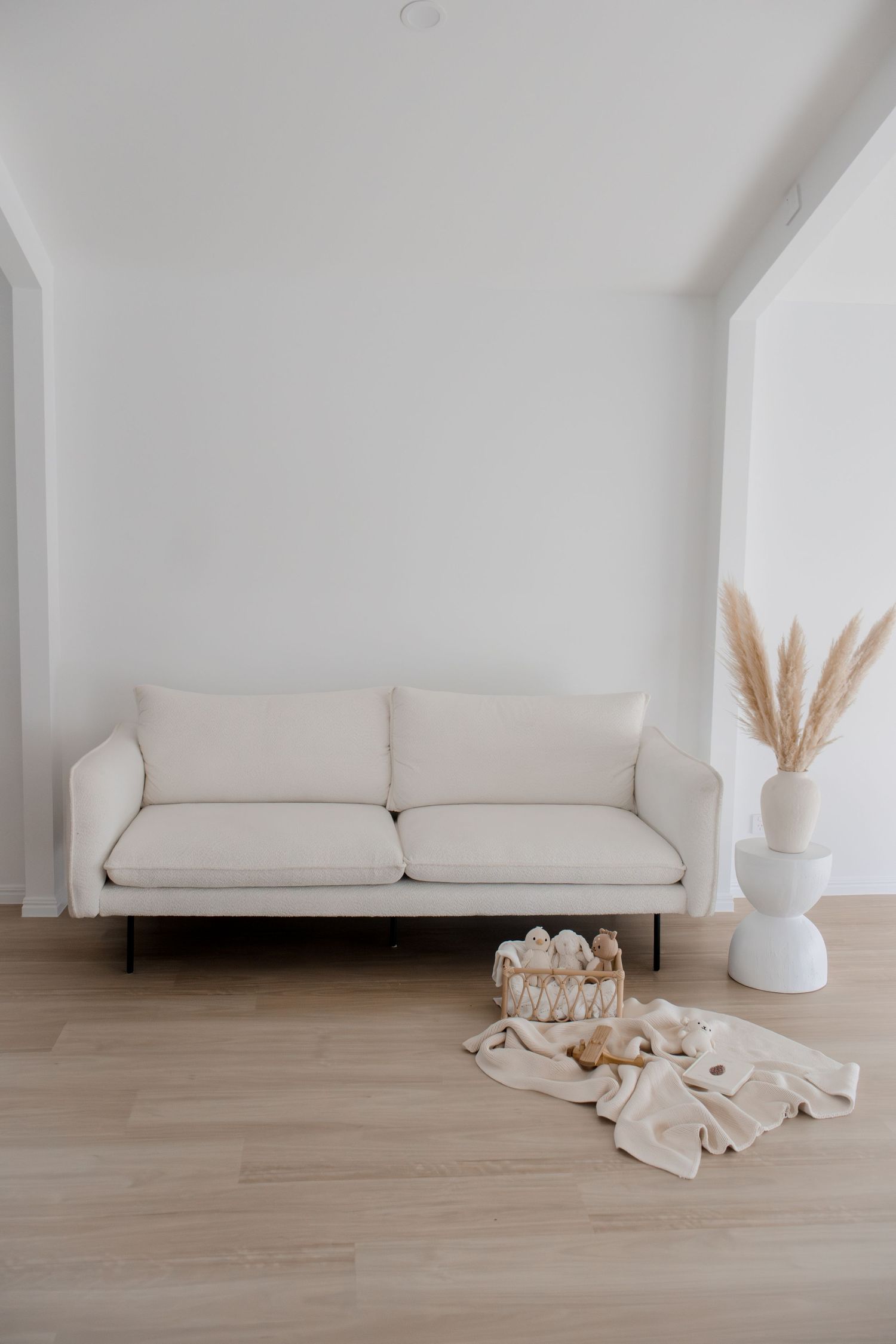 Minimalist white studio with cream sofa, pampas grass vase, and baby props on floor.