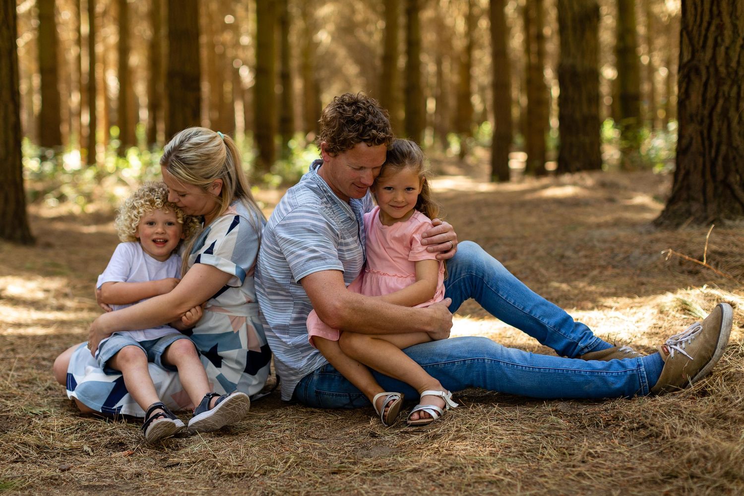 Family members lying together on fallen autumn leaves in a sunlit forest setting.