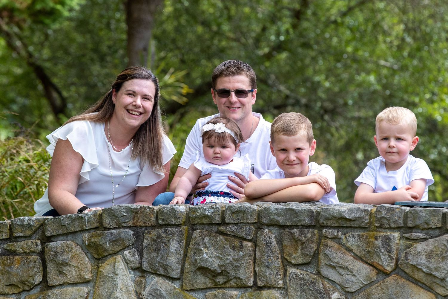 People leaning on a stone wall outdoors surrounded by lush greenery.