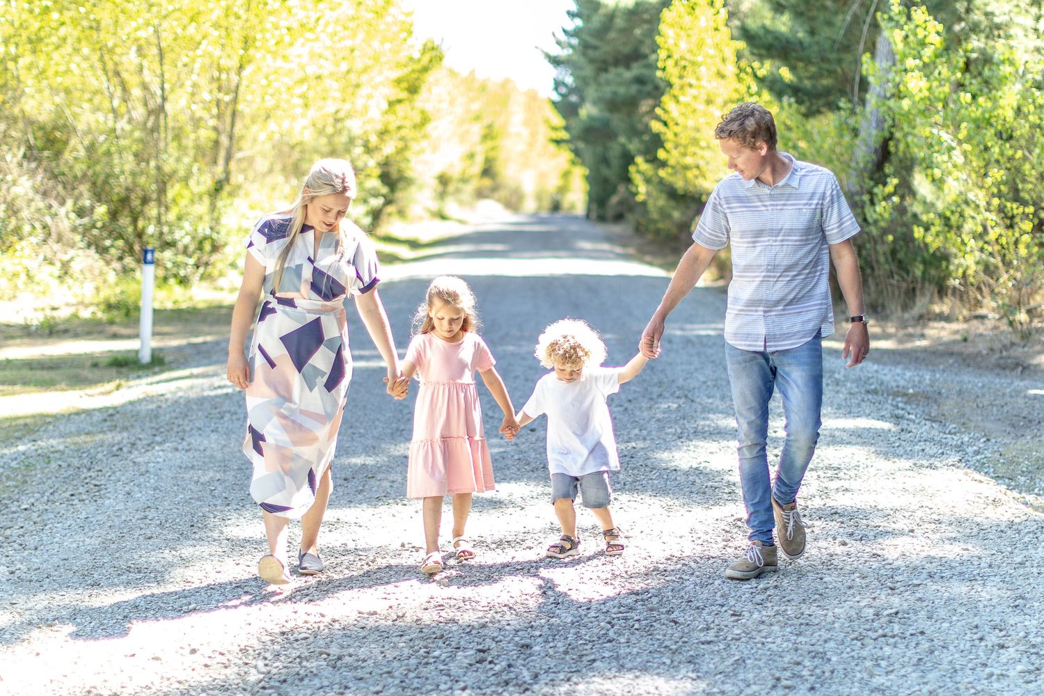 Family walking together on a gravel path through a sunny outdoor setting.