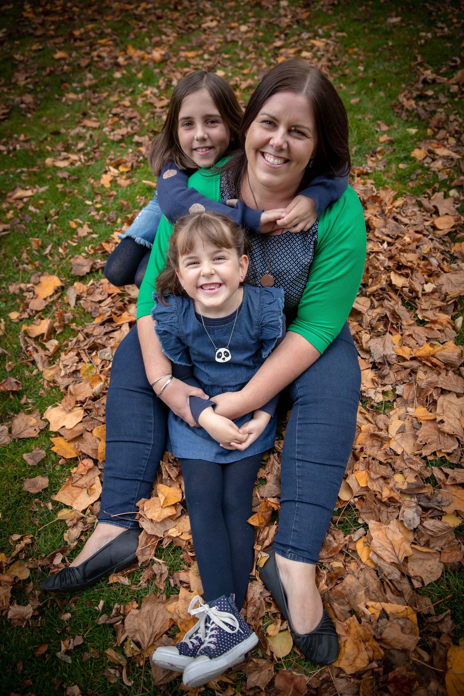 Parent and child sitting together on autumn leaves in matching denim and casual wear.