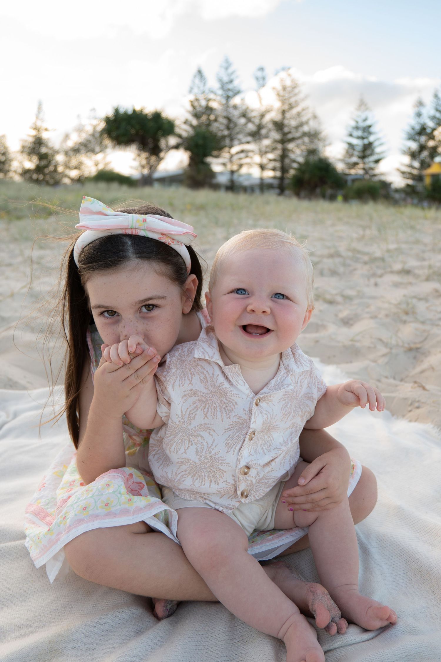 Siblings smiling and kissing hand on blanket beach golden hour family session - Photos by Bailey Rose Gold Coast
