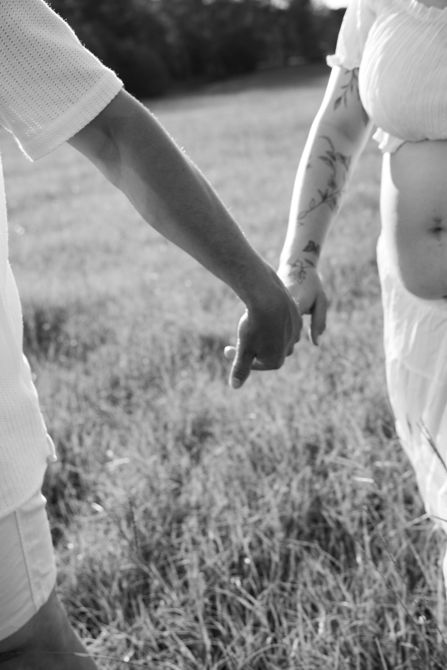 Black and white close up image of couple holding hands and walking together maternity open field - Photos by Bailey Rose Brisbane