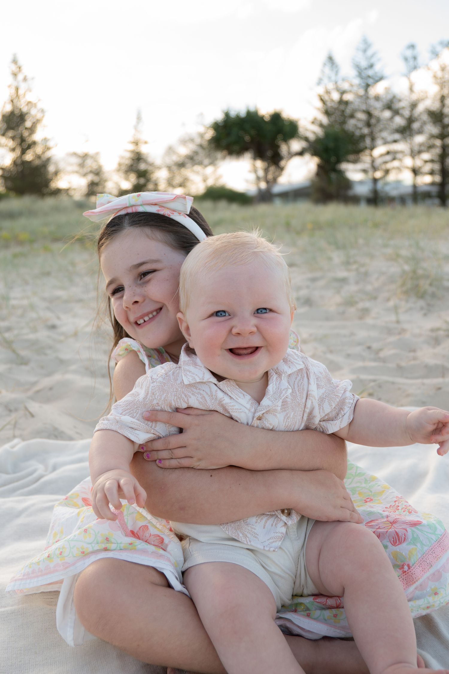 Two young siblings sitting on a blanket at the beach during sunset both laughing and smiling - Photos by Bailey Rose Gold Coast