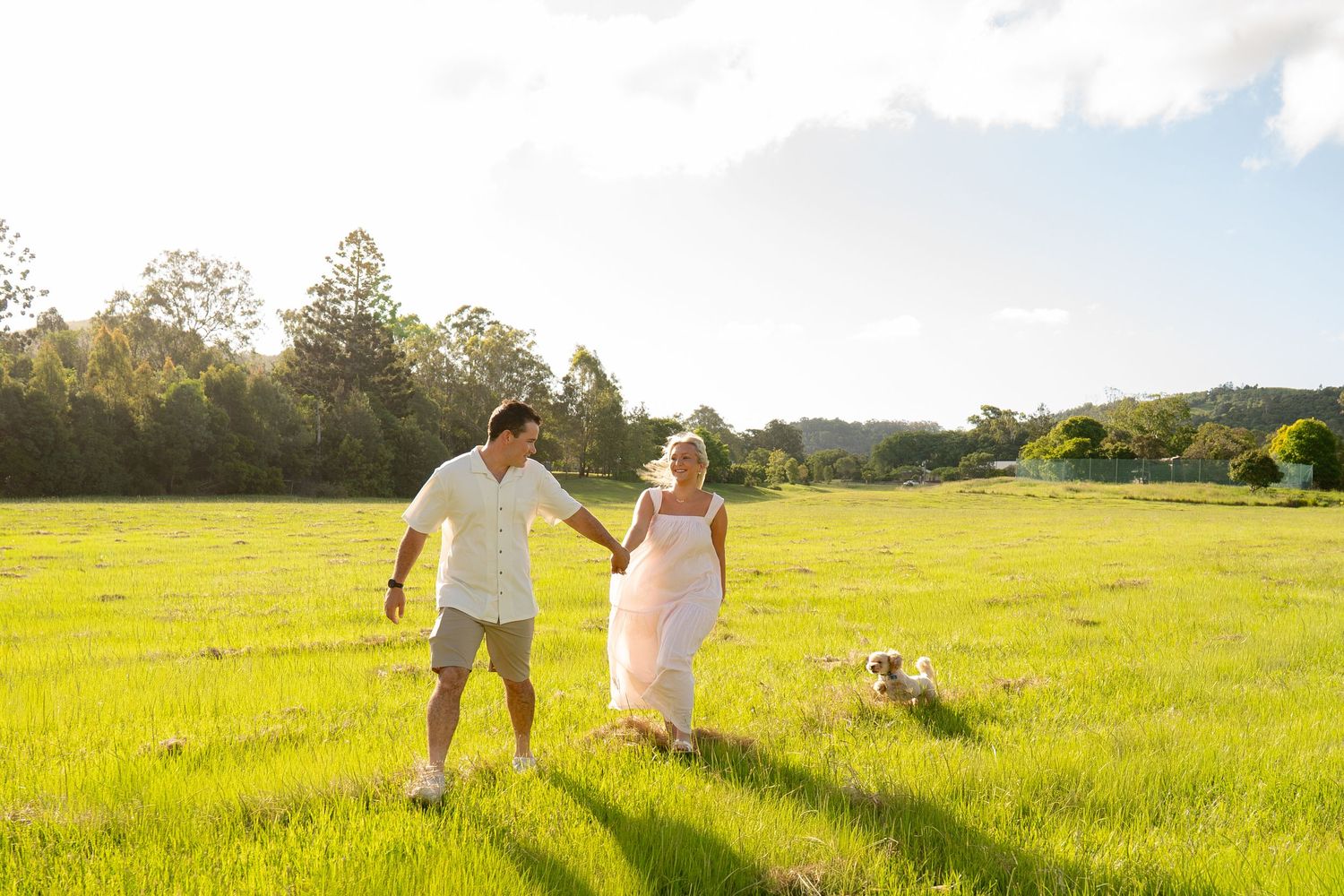 Couple holding hands walking together with puppy following in open field - Photos by Bailey Rose Gold Coast