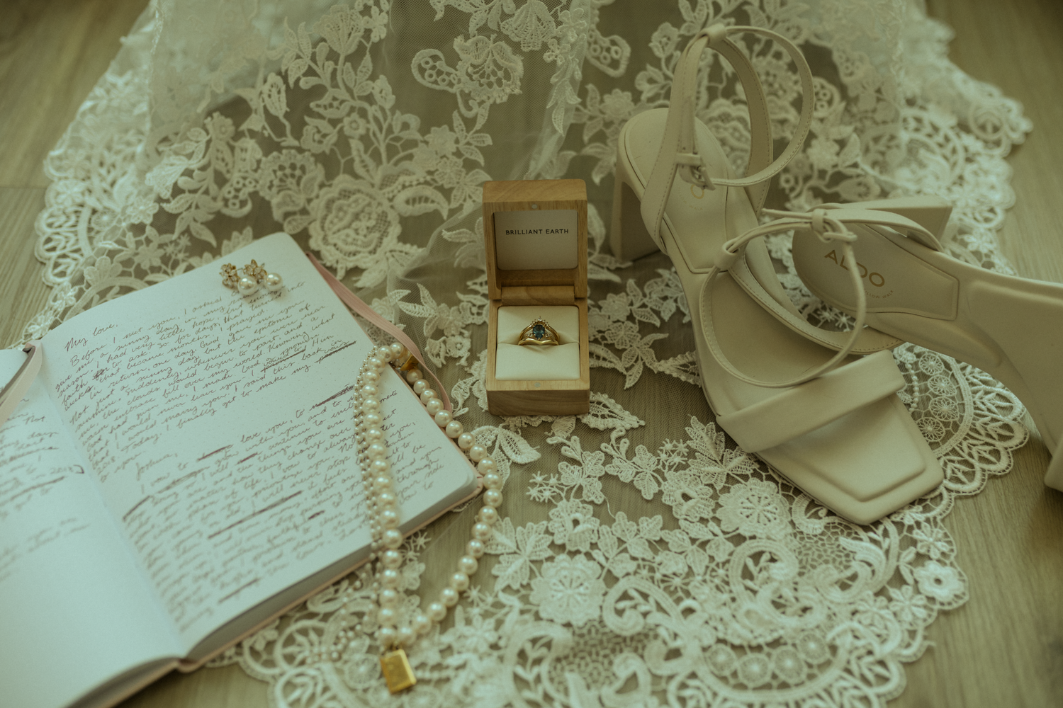 A photo of the brides details as she gets ready in the hotel room. High heels, pearl necklace, wedding ring, and vow book.