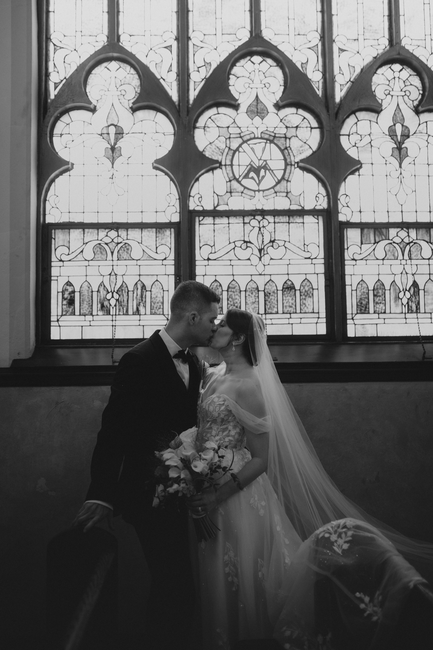 newly married couple poses in front of stained glass windows for the wedding portraits