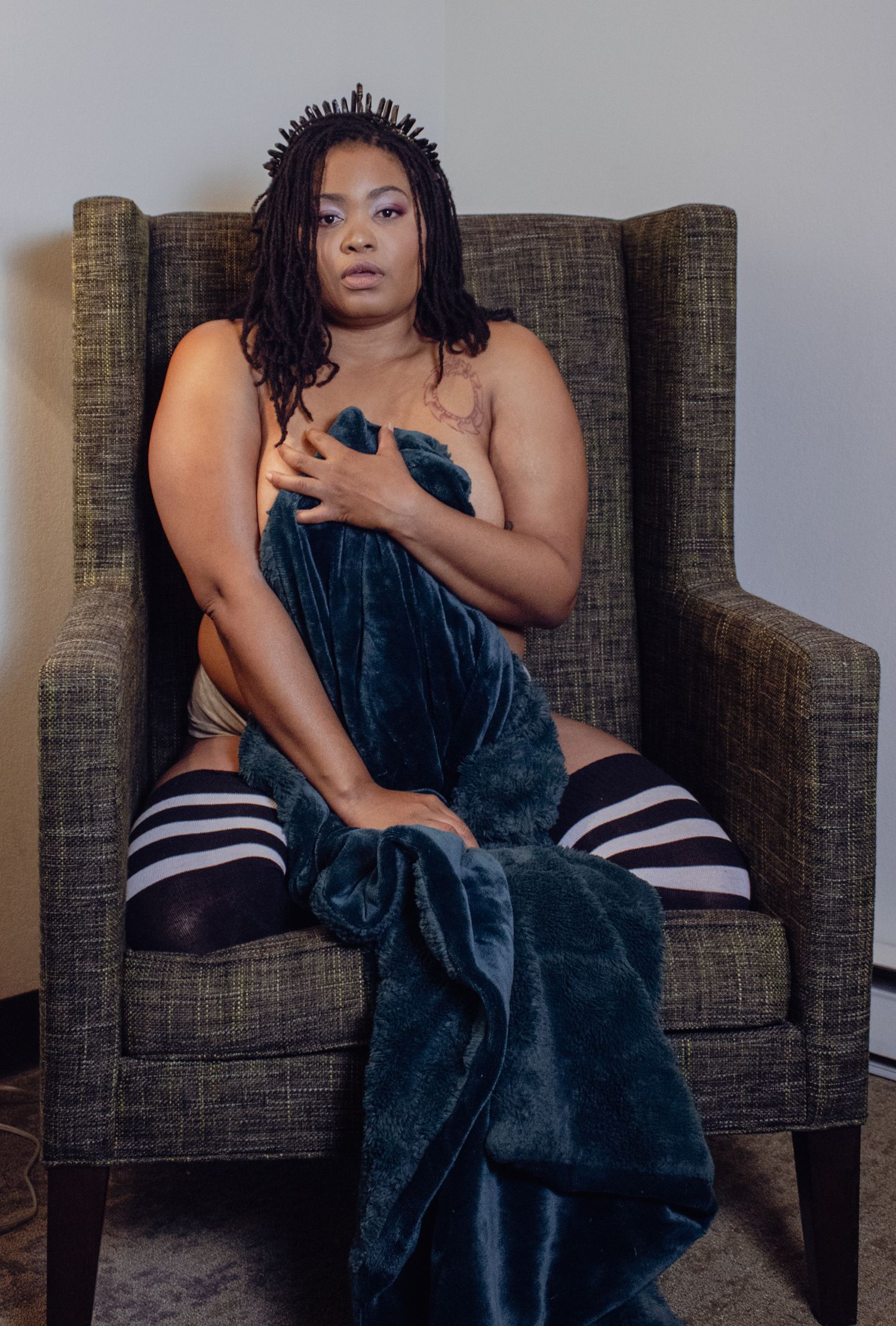 Person draped in dark velvet blanket reclines on textured gray couch.