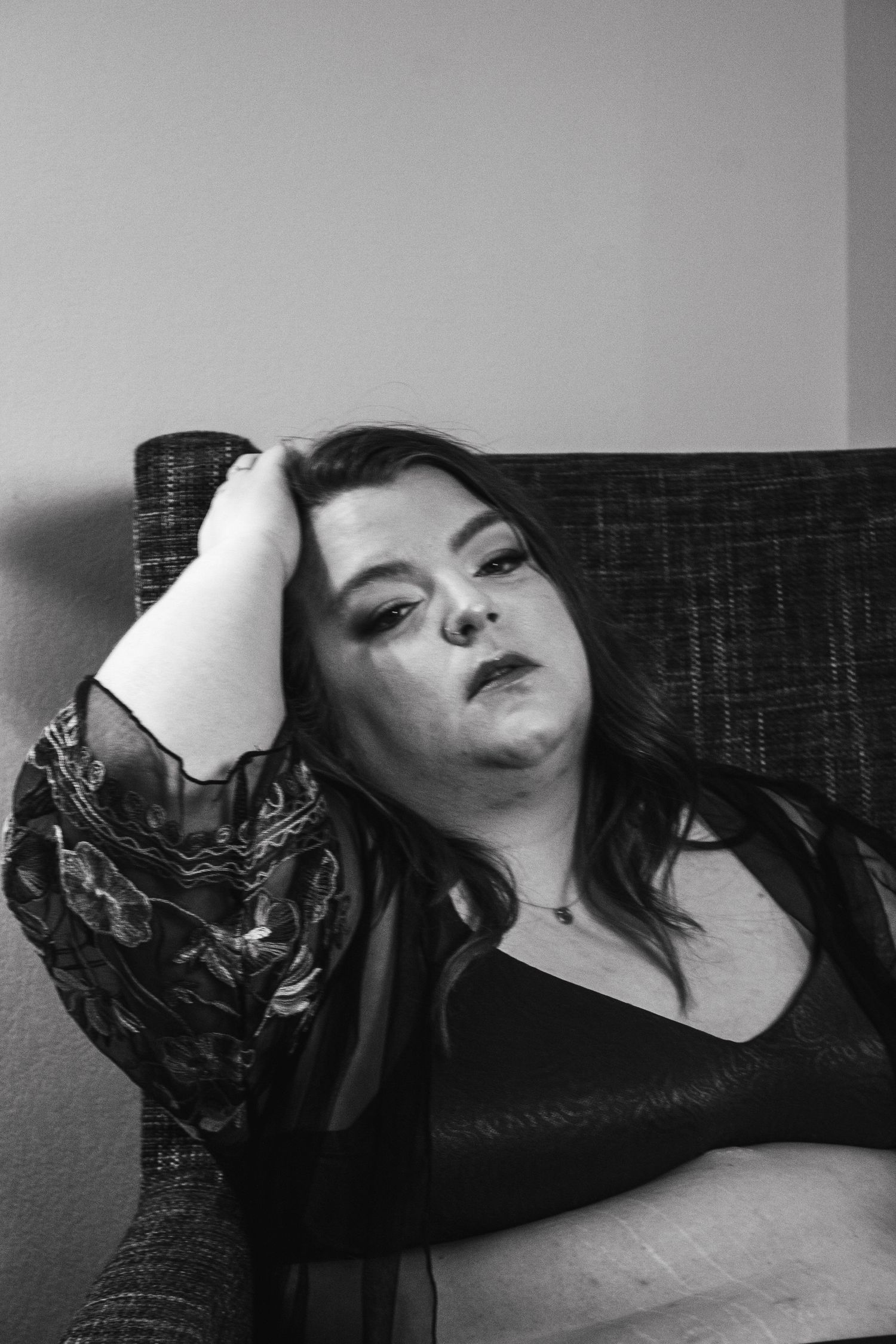 Artistic black and white portrait showing relaxed pose on dark textured couch.