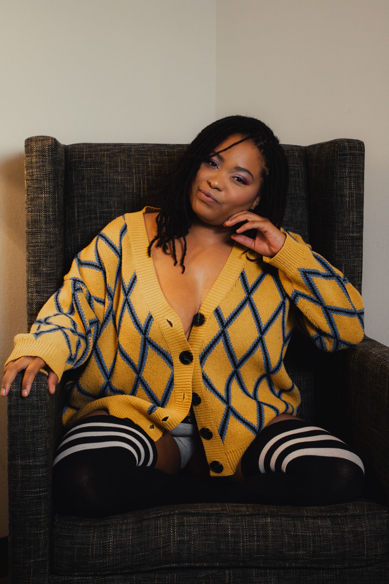 Person in yellow geometric pattern sweater poses on charcoal colored couch.