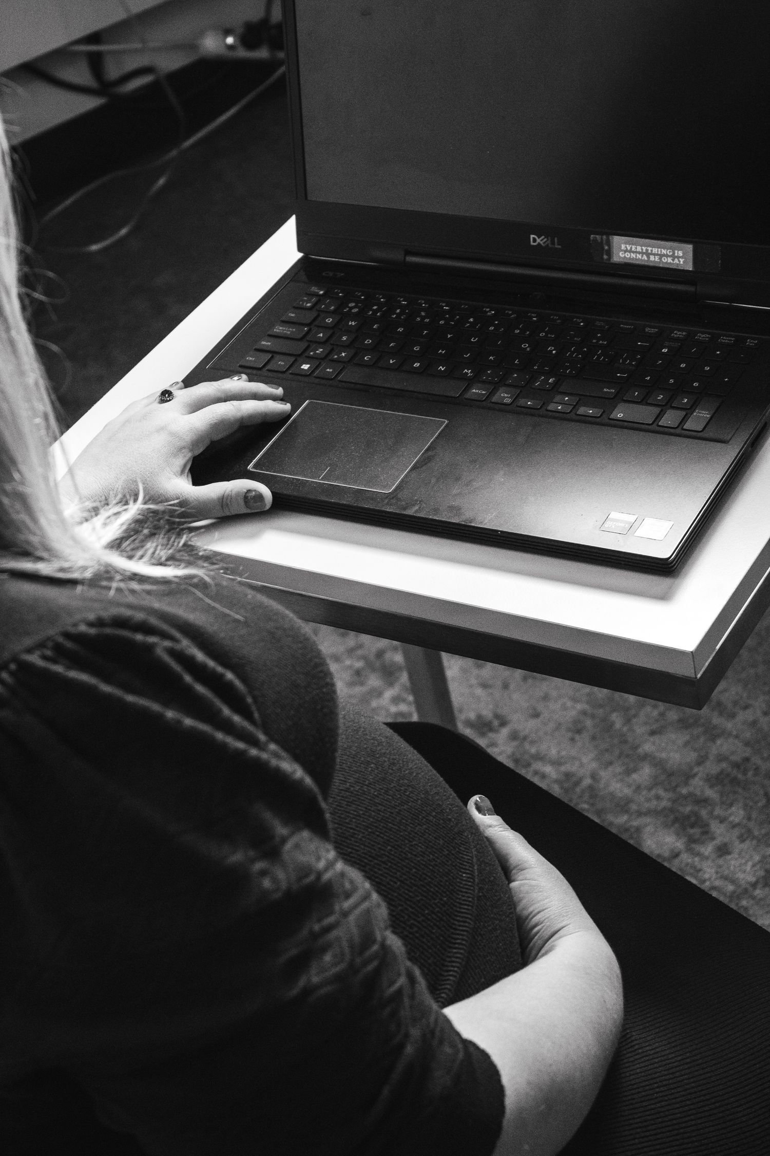 Black and white image showing hands typing on a Dell laptop keyboard.